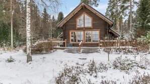 Une cabane en bois avec un toit à pignon, de grandes fenêtres et un paysage enneigé.