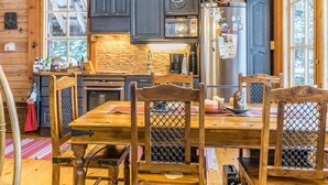 L’intérieur d’un chalet en bois comprend une table à manger, des chaises, un lustre et un coin cuisine avec des placards et des appareils électroménagers.