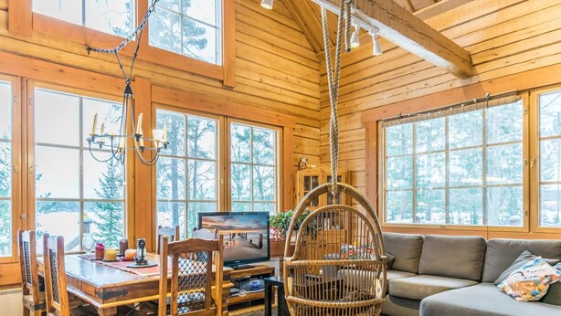 L’intérieur chaleureux d’un chalet comprend un coin repas, un téléviseur et un fauteuil suspendu.