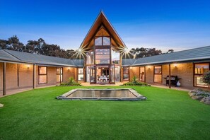 A modern house with a central glass structure, a swimming pool, and a well-maintained lawn. - Moonlight Retreat (Whittlesea)
