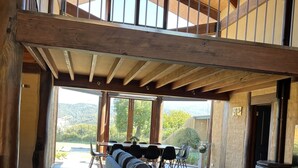 Amplia sala de estar con techo alto, vigas de madera, un sofá grande, mesa de comedor y sillas.