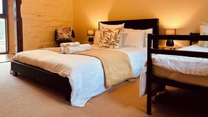 Ein Hotelzimmer mit einem großen Bett, einem kleineren Bett, zwei Nachttischen mit Lampen, einem Fenster mit Vorhängen und einer Steinwand.