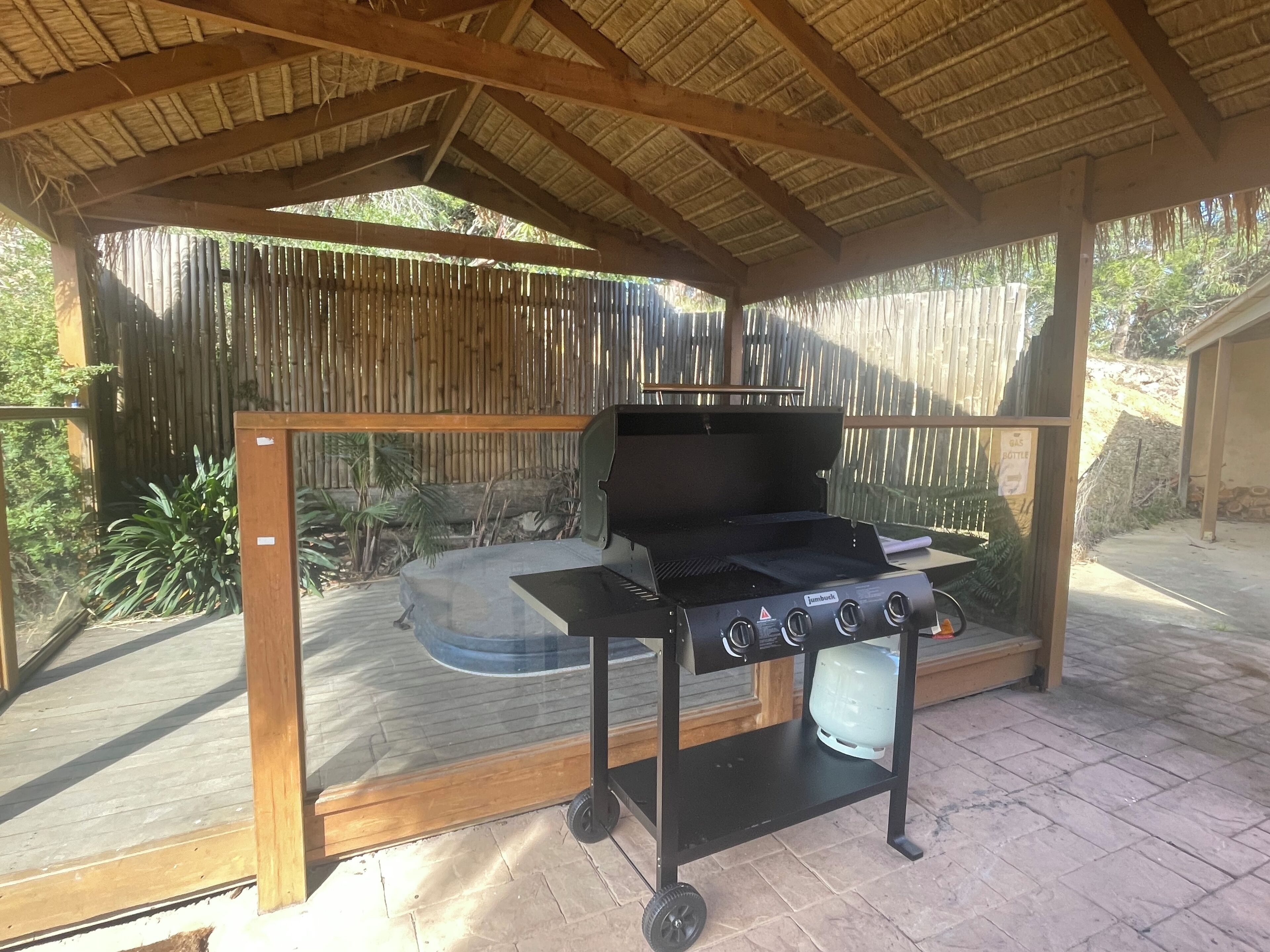 Una barbacoa sota una pérgola de fusta amb una tanca de bambú al fons.
