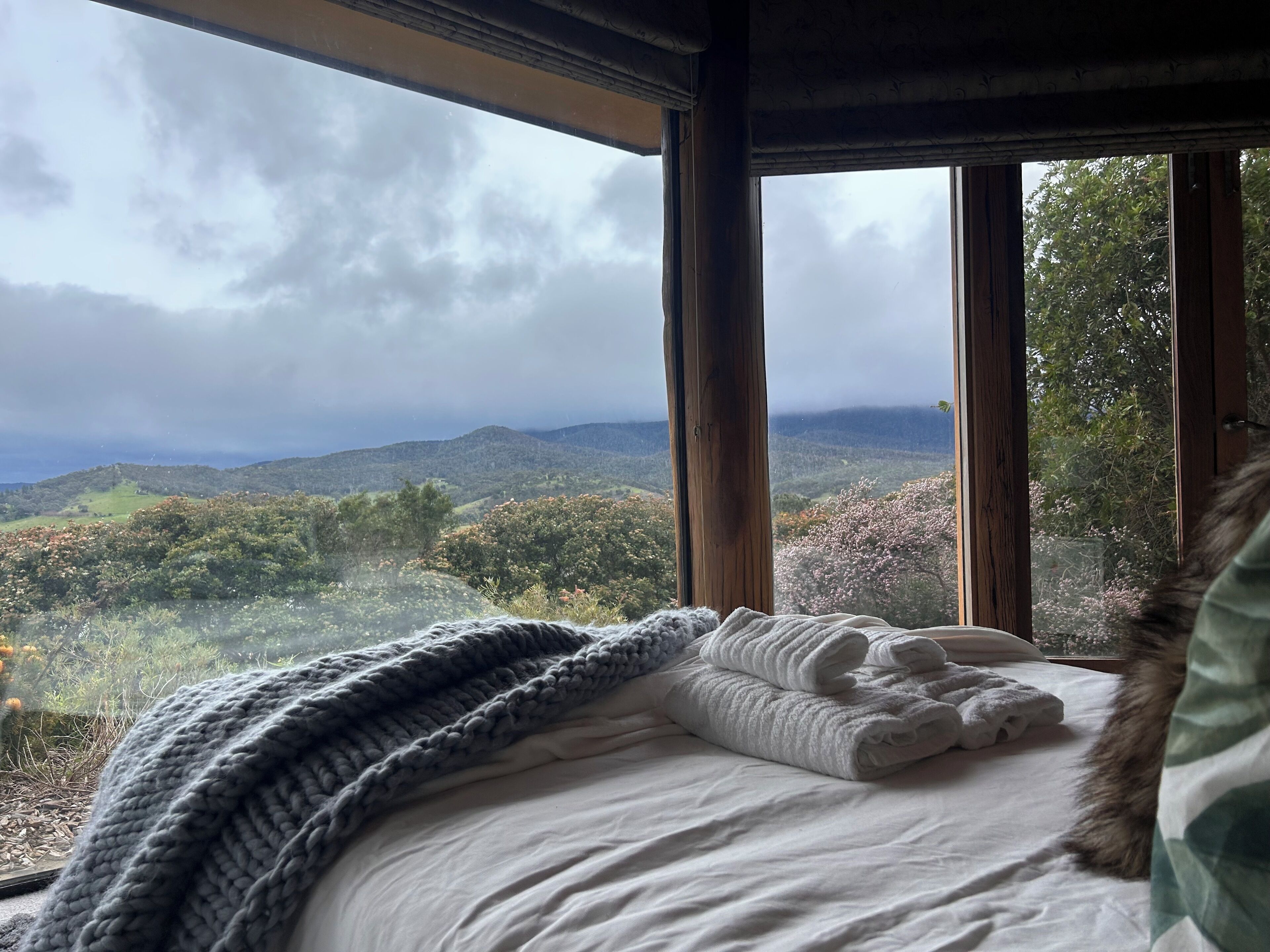 Una cama con vista a un paisaje montañoso a través de amplios ventanales.