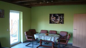 Un coin repas avec une table dressée pour quatre personnes, entourée de quatre chaises, un plafond en bois et un mur vert.