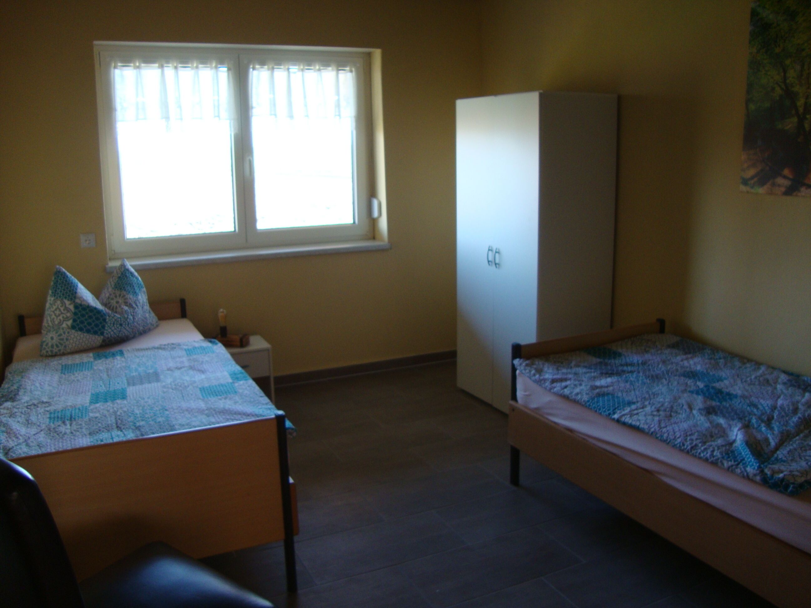 Een kamer met twee bedden, een kledingkast, een raam met gordijnen en een klein tafeltje.