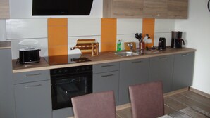 Une cuisine moderne avec des meubles gris, une hotte noire, un four encastré, une machine à café et une planche à découper en bois.