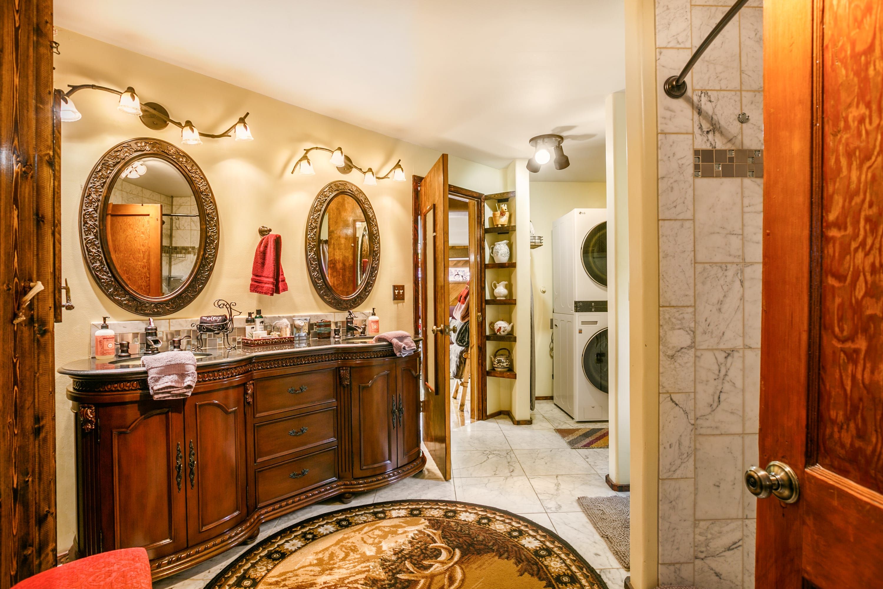 A bathroom with a wooden vanity, two large mirrors, a towel rack, and a shower area.