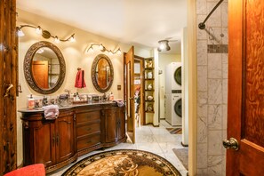 Ein Badezimmer mit einem Holzkosmetikschrank, zwei großen Spiegeln, einem Handtuchhalter und einer Duschkabine.