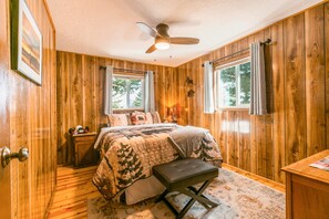 Une chambre à coucher aux murs lambrés, avec un lit, un banc, une table de chevet et un ventilateur de plafond.