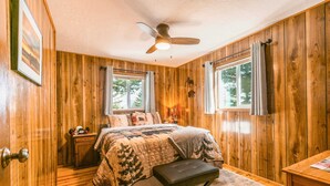 Ein Schlafzimmer mit Holzwandverkleidung, einem Bett, einem Nachttisch, einer Bank und einem Deckenventilator.