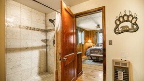 Un baño con ducha, una puerta de madera, una cama con edredón estampado y un calentador de pared.