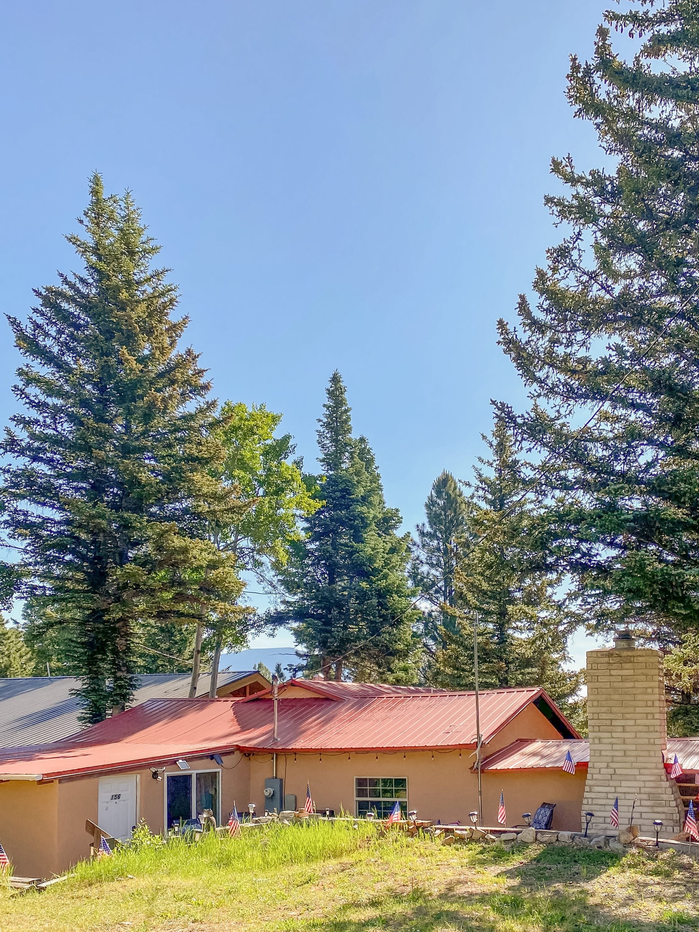 A building with a red roof, surrounded by tall trees, and a clear sky.