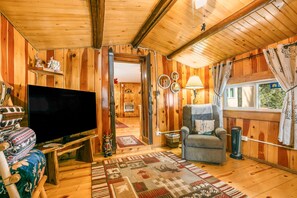 A cozy cabin interior with a large flat-screen TV, a comfortable armchair, a patterned rug, and a window with curtains. - Medallion Cabin by Velo (Eagle Nest)
