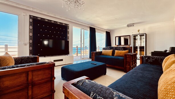 Un salon doté d’un grand téléviseur, de canapés et offrant une vue sur la mer.