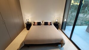 A modern bedroom with a large bed, two bedside tables with lamps, a wardrobe, and a large window with a view of greenery. - Maison D'architecte 2024, Lecci Corse,15 mn de Porto-vecchio - Proche mer (Lecci)