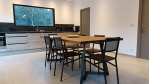 A modern kitchen with a large island, dark cabinetry, and a view of trees through a window. - Maison D'architecte 2024, Lecci Corse,15 mn de Porto-vecchio - Proche mer (Lecci)