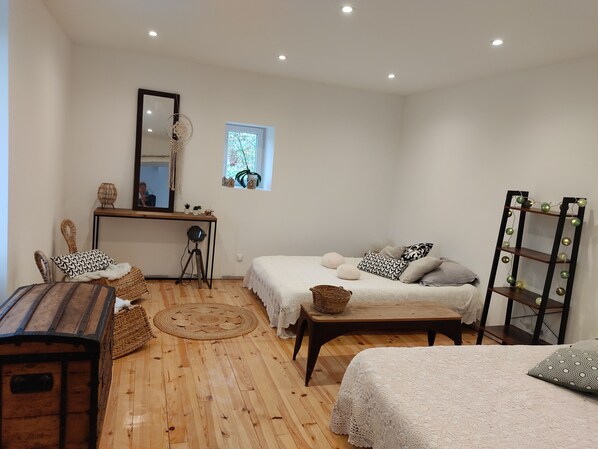 A cozy room with a wooden floor, a bed with white bedding, a desk with a mirror, and a small window with a plant.