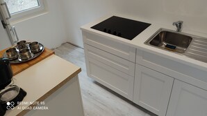 A modern kitchen with a white countertop, a black induction cooktop, a stainless steel sink, and a window with a view of greenery outside. - Maisonnette a la Campagne au Calme (Broquiès)