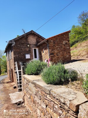 A rustic stone house with a small porch, a wooden staircase, and a thatched roof.