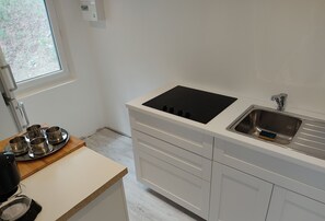 Eine moderne Küche mit weißer Arbeitsplatte, einer schwarzen Induktionskochplatte, einem Edelstahl-Spülbecken und einem Fenster mit Blick auf Grünflächen.
