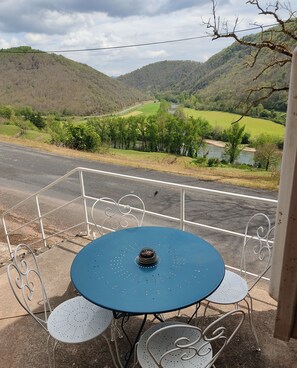 Ein Tisch und Stühle auf einem Balkon mit Blick auf einen Fluss und Hügel.