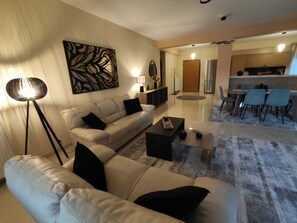 A modern living room with a sofa, coffee table, and floor lamp. There is a dining area with chairs and a table. A kitchen is visible in the background. - Sunset view  (Ioannina)