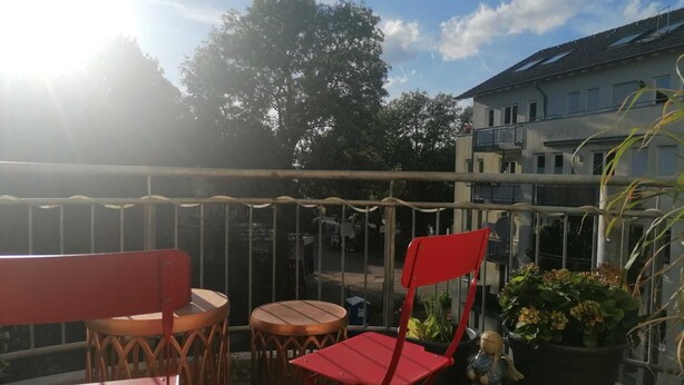A balcony with a table and chairs, a potted plant, and a view of a building in the background.