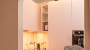 A compact kitchen with white cabinets, a wooden countertop, a kettle, a toaster, and a bar stool.