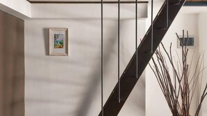 Een moderne trap met een minimalistisch ontwerp, een ingelijst kunstwerk aan de muur en een vaas met takken.
