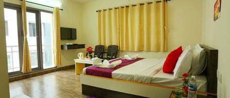 A hotel room with a bed, a desk, a chair, a television, and a window with curtains.