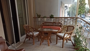 Un balcon agrémenté de meubles en osier, d’une table en verre et de plantes en pot.