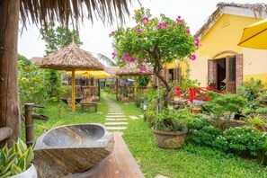 Stroll through the lush garden, featuring a pathway leading to a charming guesthouse surrounded by potted plants and flowering trees.
