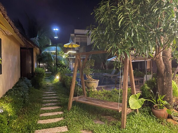 Stroll through the serene garden pathway to the inviting entrance, surrounded by lush greenery and potted plants.