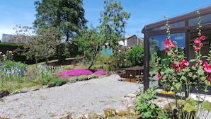 Un jardín con senderos de grava, diversas plantas florecientes y un banco de madera.