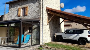 Una casa de piedra con un porche acristalado, un SUV blanco estacionado afuera y un pérgola de madera.