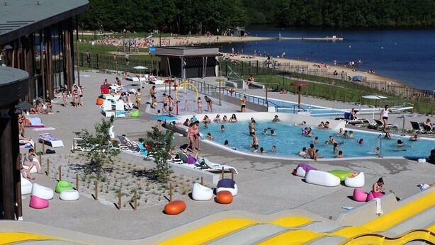Un área de piscina con varias piscinas, sillas de descanso y toboganes acuáticos.