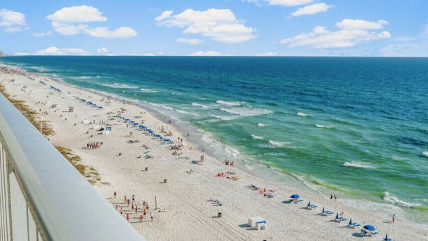 A beach with a long stretch of sand, umbrellas, and people.