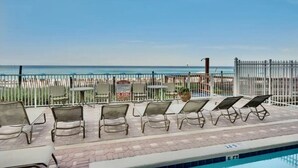 A poolside area with lounge chairs and a view of the ocean.