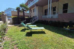 A courtyard with two lounge chairs, a staircase, and a building with balconies.
