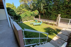 A backyard with a lawn, two green lounge chairs, a white fence, and a stone pillar.