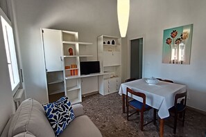 A compact living space with a sofa, a dining table with chairs, a TV, and built-in shelving.
