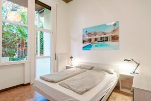 Ein Schlafzimmer mit einem Bett, zwei Nachttischen, einem Fenster mit Blick auf Grünflächen und einem Bild von einem Schwimmbad.