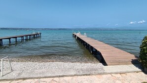Una vista despejada de un muelle de madera que se adentra en aguas tranquilas, con una costa rocosa y tierra firme a lo lejos.