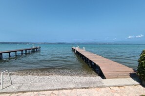 Ein klarer Blick auf einen hölzernen Steg, der sich in ruhiges Wasser erstreckt, mit einer felsigen Küste und weiter hinten Land.