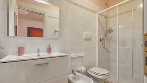 Ein Badezimmer mit Dusche, Toilette, Bidet und einem Waschtisch mit Schubladen und Spiegel.