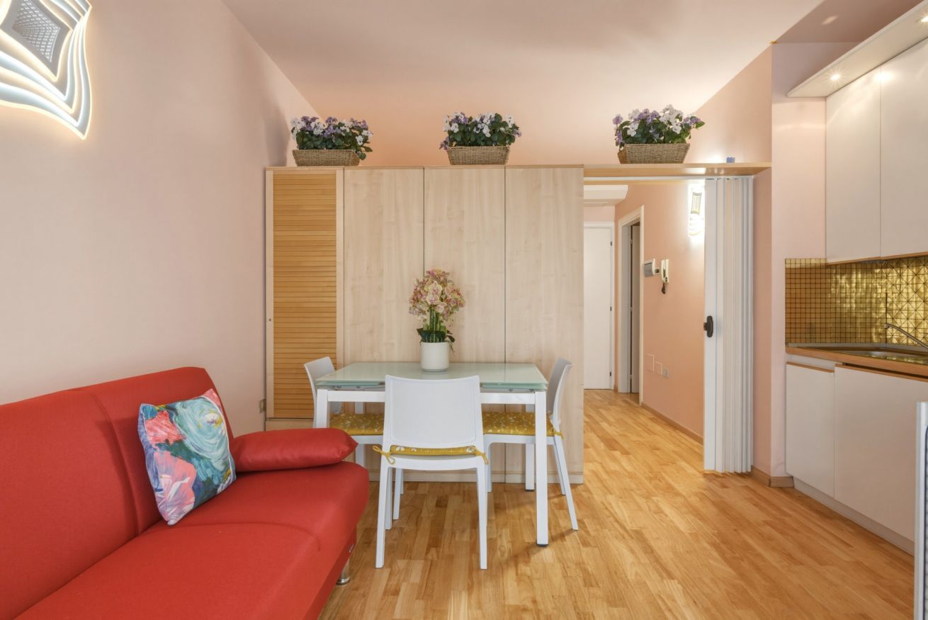 Un espacio habitable compacto con una mesa de comedor, sillas, un sofá rojo y una zona de cocina con armarios y encimera.