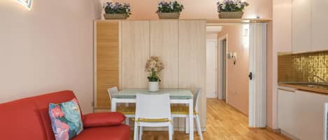 A compact living space with a dining table, chairs, a red sofa, and a kitchen area with cabinets and a countertop.