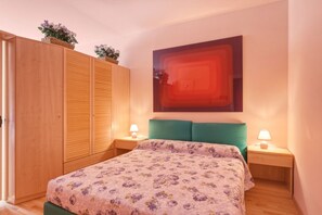 Ein Schlafzimmer mit Bett, Holzschrank, zwei Nachttischen mit Lampen und einem Wandbild.