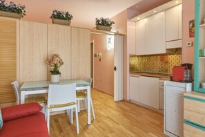 A compact kitchen with wooden cabinets, a dining table with chairs, and a small refrigerator.